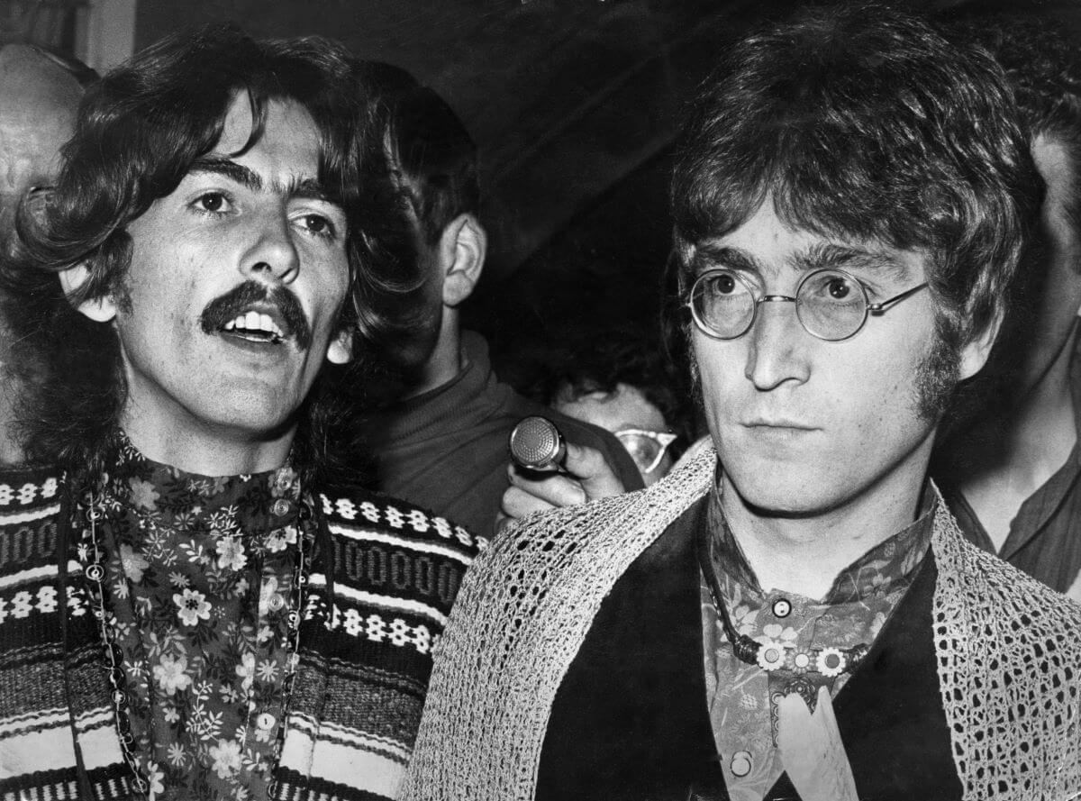 A black and white picture of George Harrison and John Lennon walking through a crowd. 