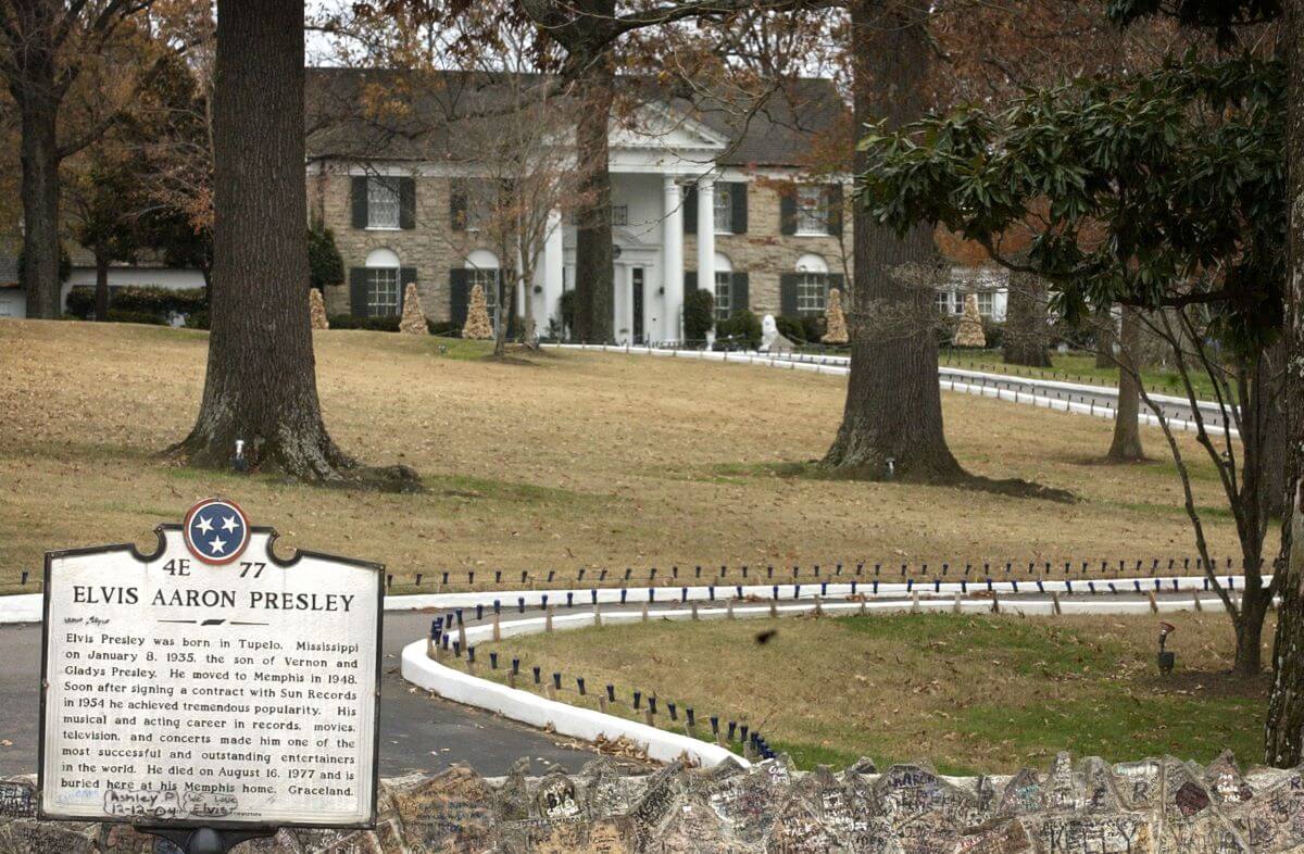 Graceland and its front drive are pictured behind a sign giving a brief biography of Elvis' life.