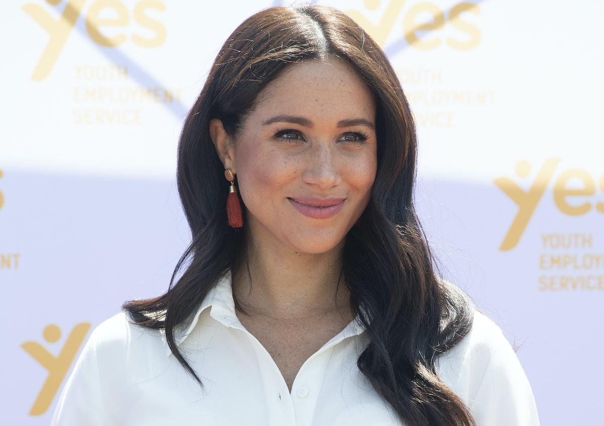 Meghan Markle smiling and wearing a white blouse in 2019.