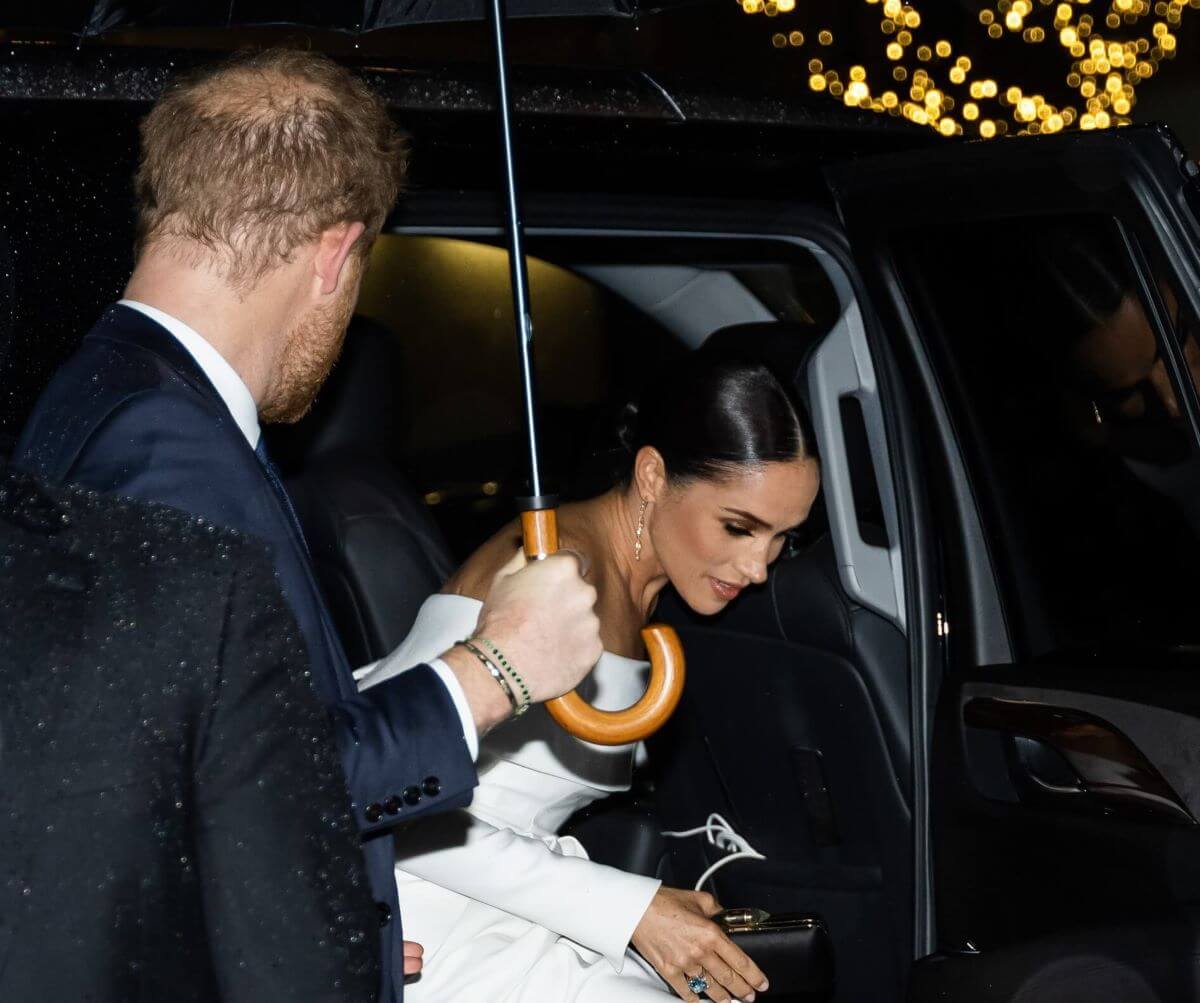 Prince Harry, who a body language expert says has become just part of Meghan Markle's entourage which could signal trouble in their marriage, holds an umbrella for his wife as they arrive at the Ripple of Hope Award Gala