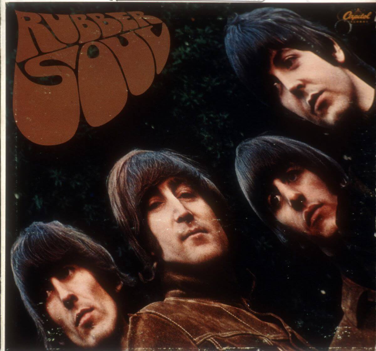 The album cover for The Beatles' 'Rubber Soul.' George Harrison, John Lennon, Ringo Starr, and Paul McCartney pose in a diagonal line across the cover. 'Rubber Soul' is in the upper right corner.