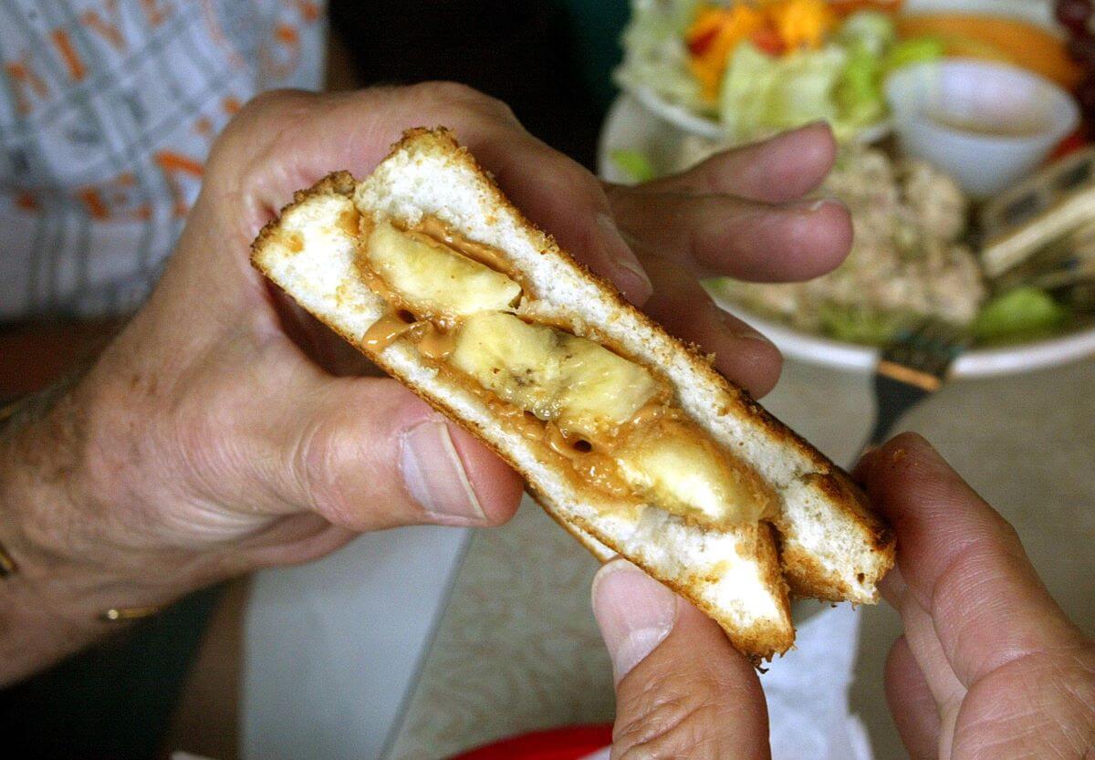 Two hands hold a peanut butter and banana sandwich, a typical Elvis Presley dinner.
