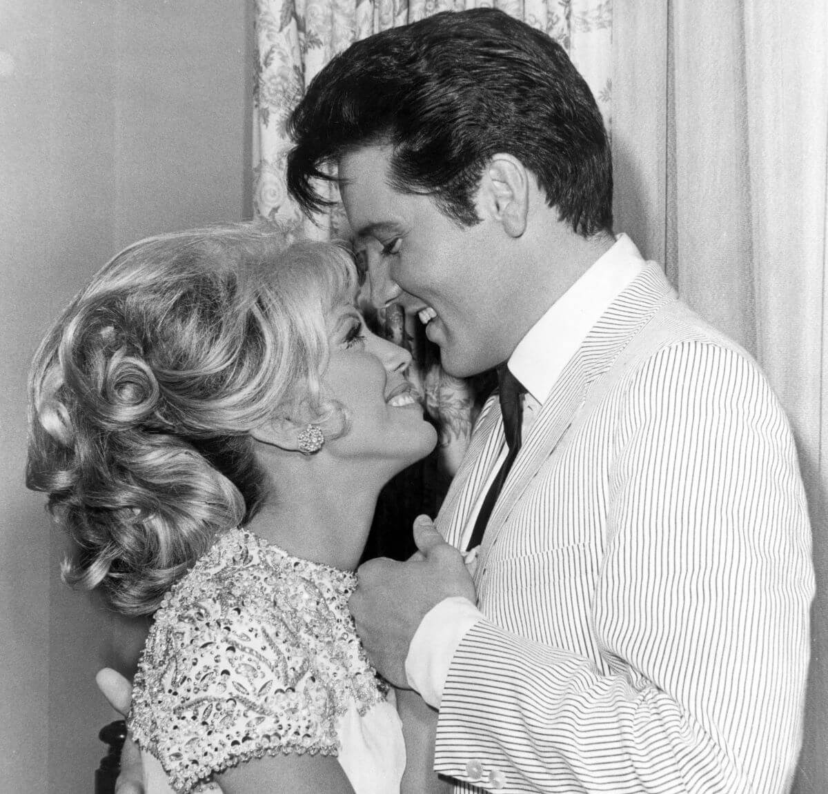 A black and white picture of Nancy Sinatra and Elvis Presley standing facing each other, close together.