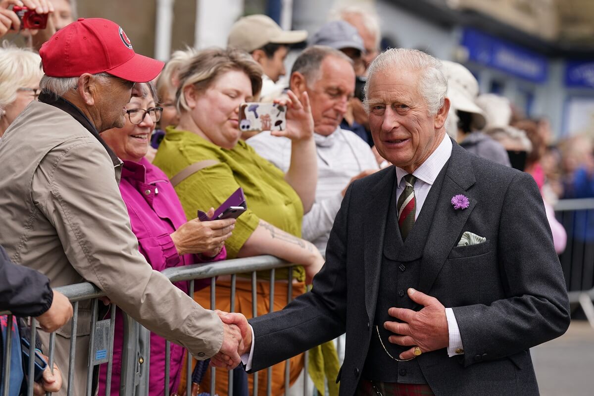 King Charles III, who a body language expert says uses Queen Camilla as a 'forcefield' during public events, speaks with well wishers in Selkirk, Scotland