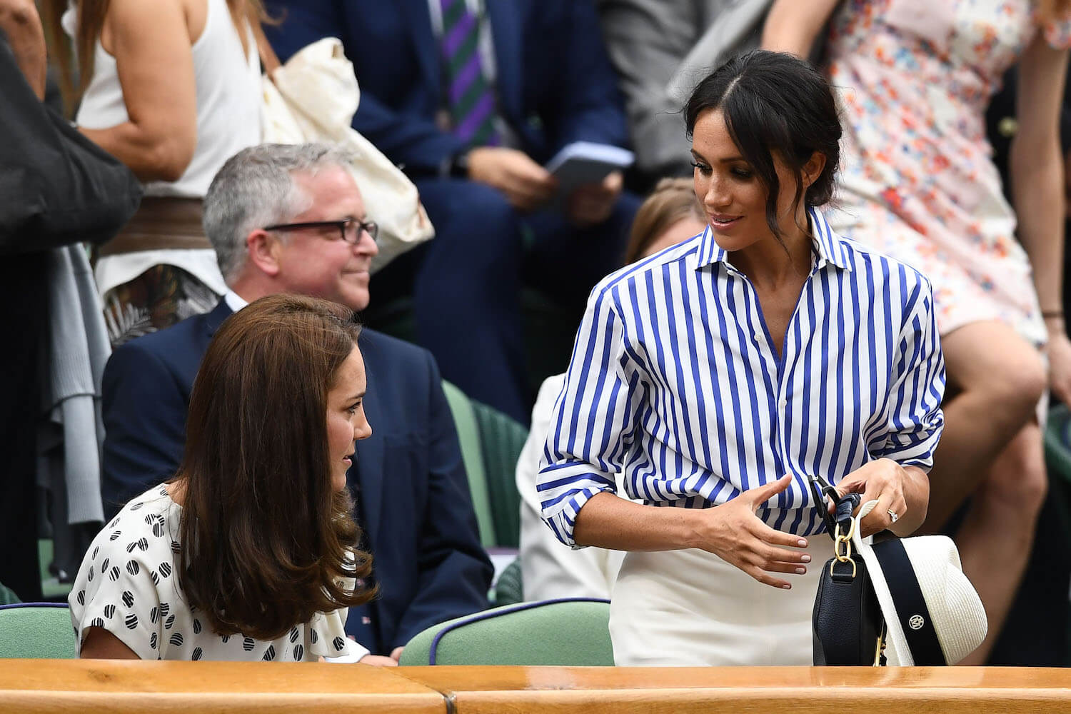 Meghan Markle in a blue striped shirt at Wimbledon standing next to Kate Middleton, who is sitting