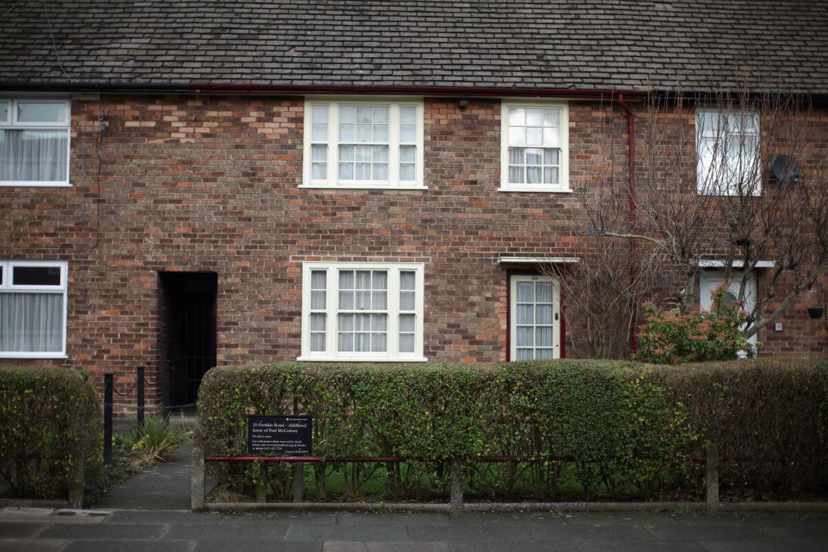 Paul McCartney's childhood home. It is a brown brick building with two stories and bushes out front.