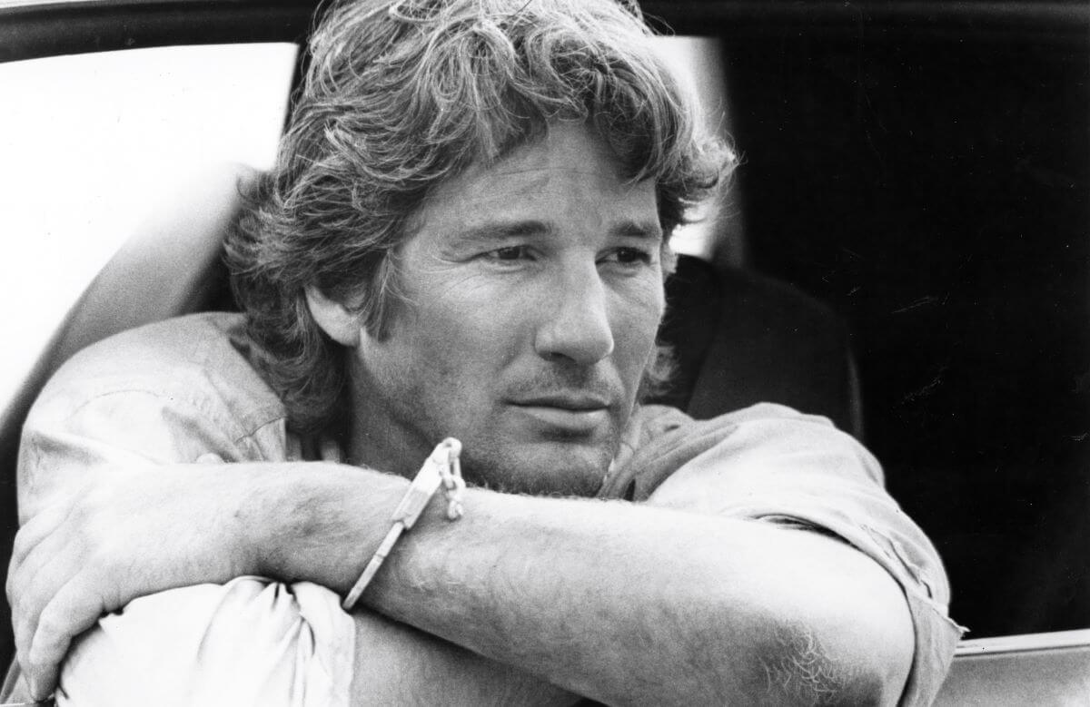 A black and white picture of Richard Gere resting his head on his crossed arms.