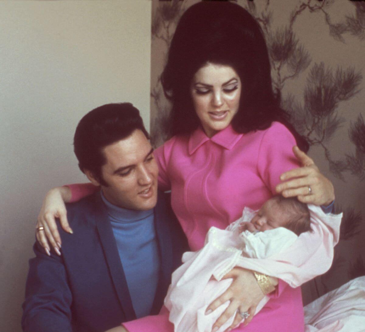 Priscilla Presley sits on Elvis Presley's lap and holds an infant Lisa Marie Presley.