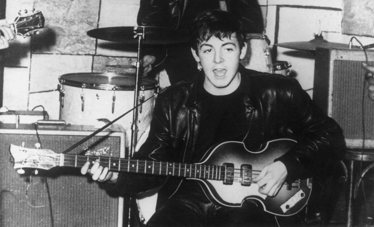 A black and white picture of Paul McCartney singing and strumming a guitar in front of a drum set.