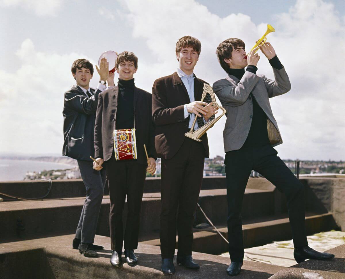 The Beatles stand on a rooftop with small instruments.