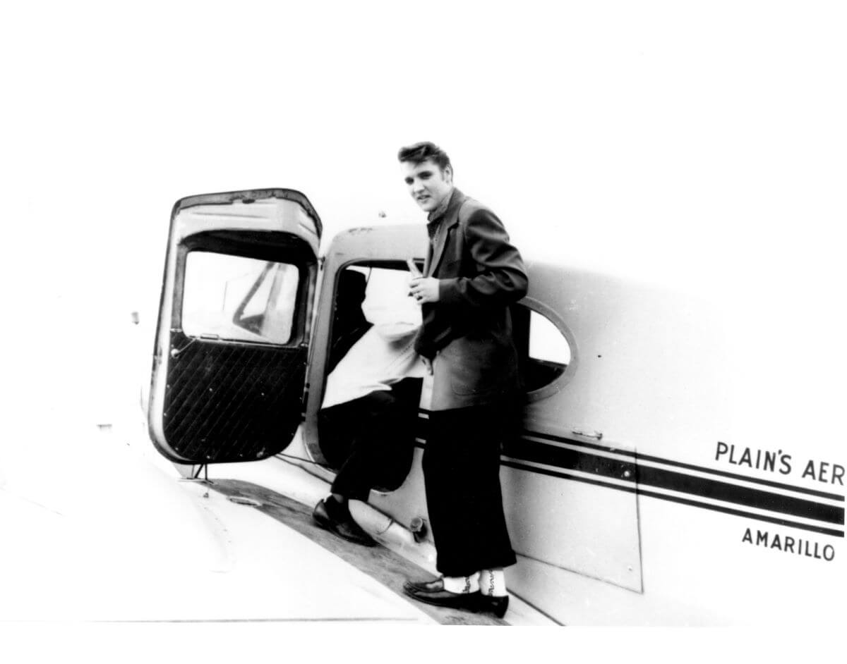 A black and white picture of Elvis preparing to board a small plane.
