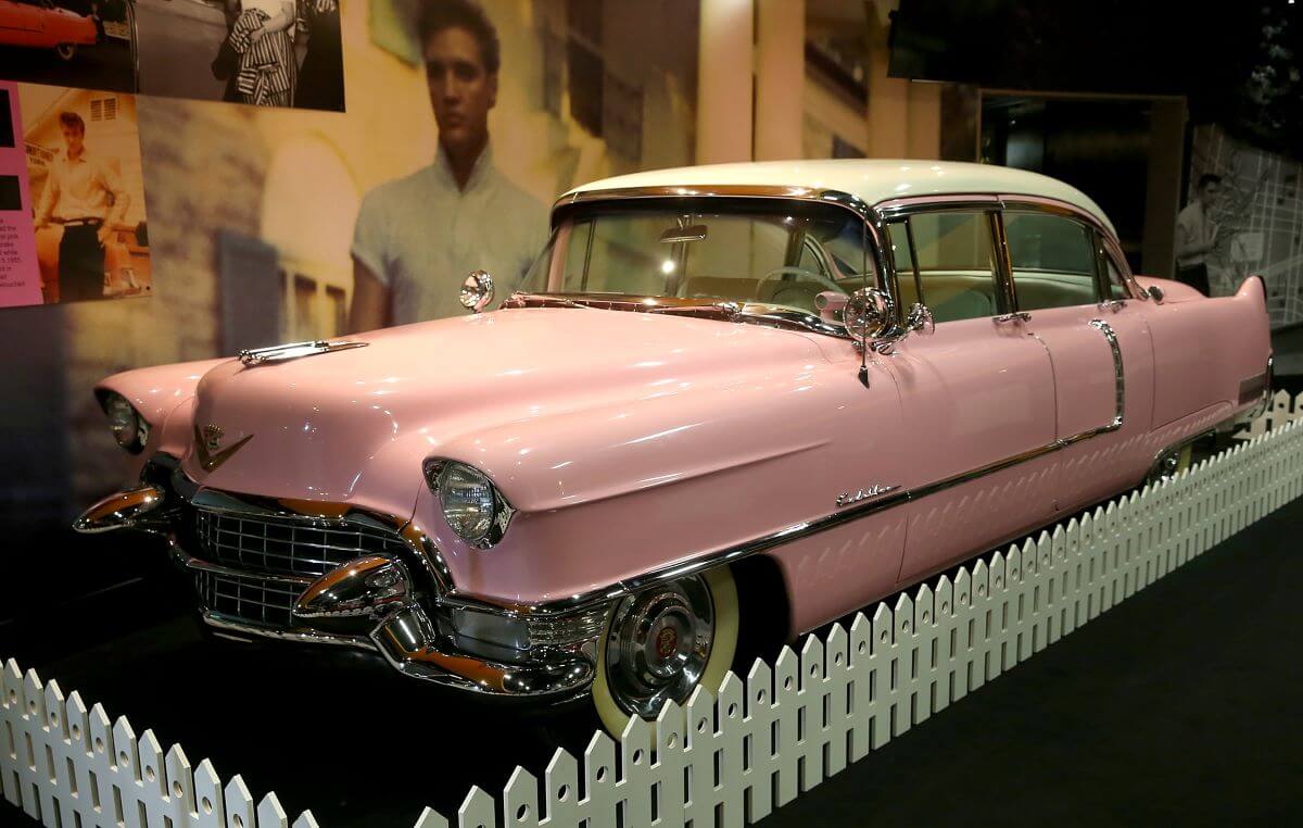 A pink Cadillac with a white roof is surrounded by white fencing.