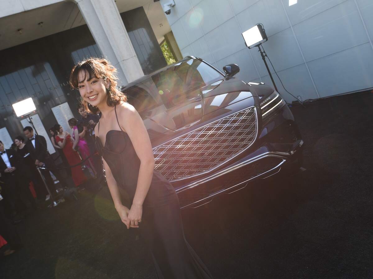 Wearing a black dress, Aubrey Anderson-Emmons poses alongside a black car at a media event