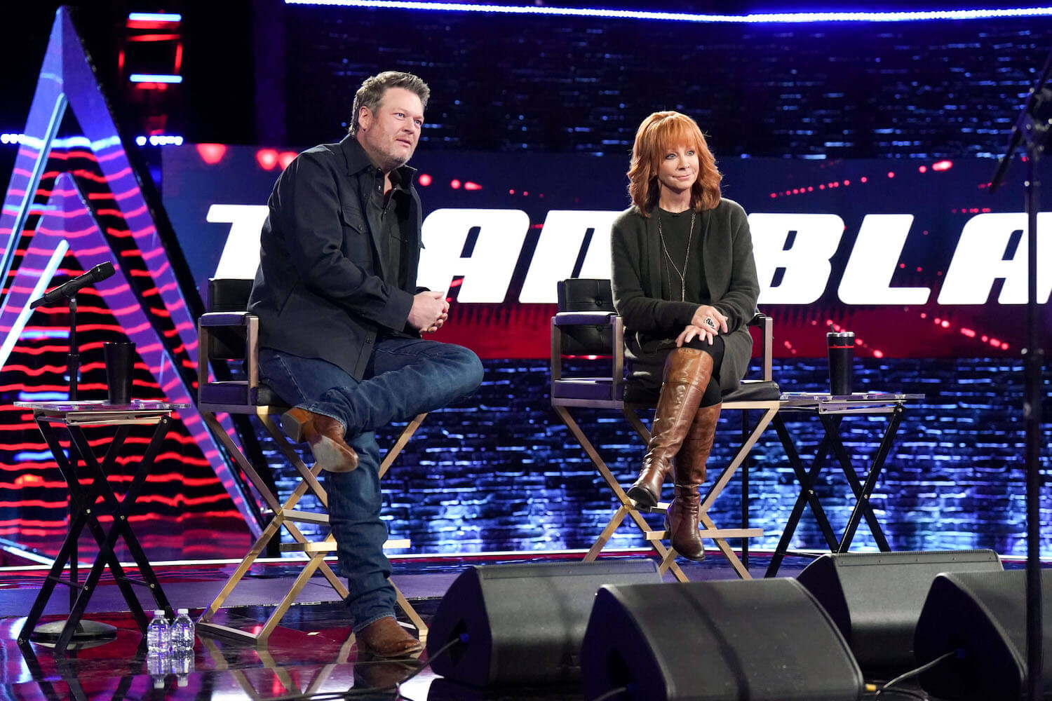 Blake Shelton and Reba McEntire sitting next to each other on 'The Voice' with a 'Team Blake' sign behind them