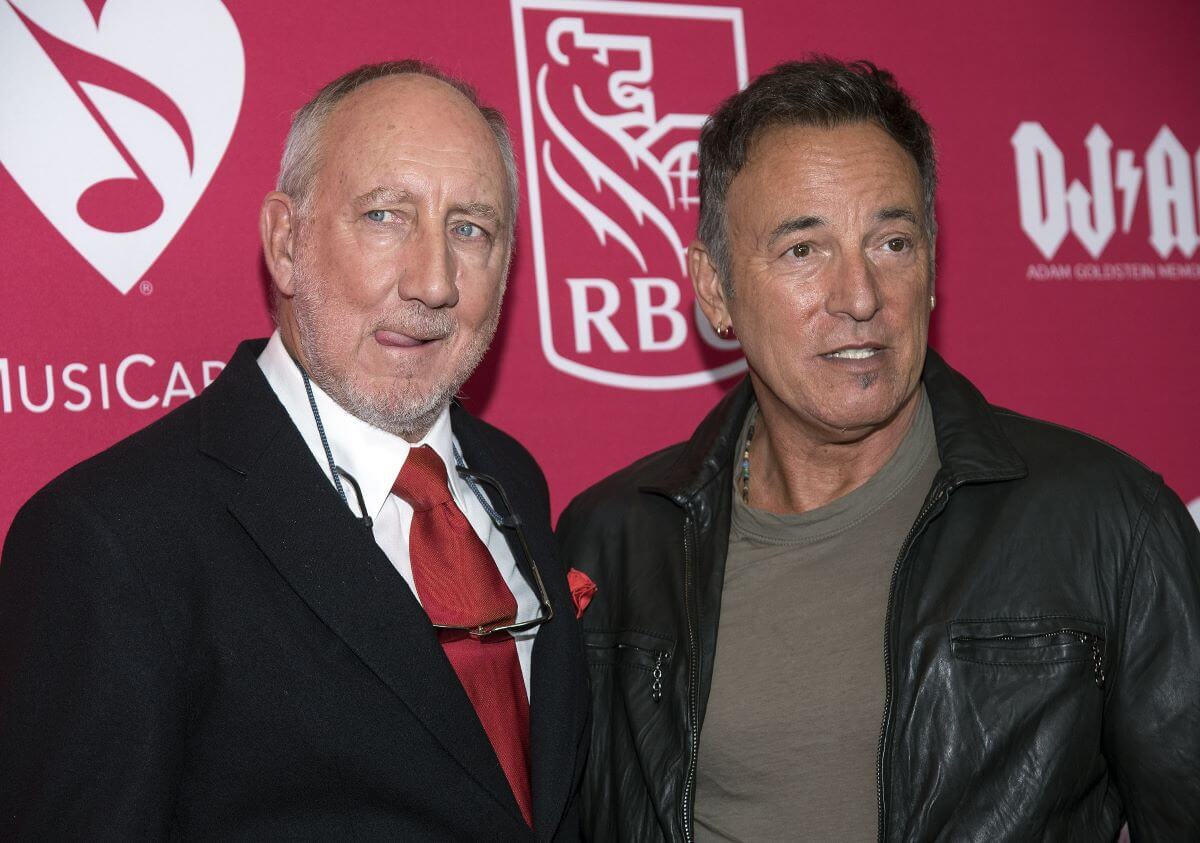 Pete Townshend and Bruce Springsteen stand next to each other in front of a red background.