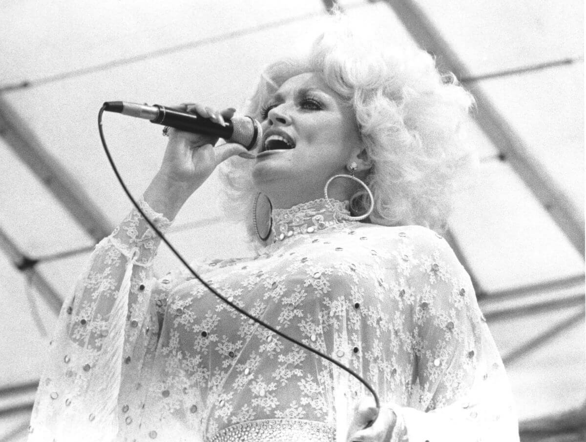 A black and white picture of Dolly Parton wearing lace and singing into a microphone.