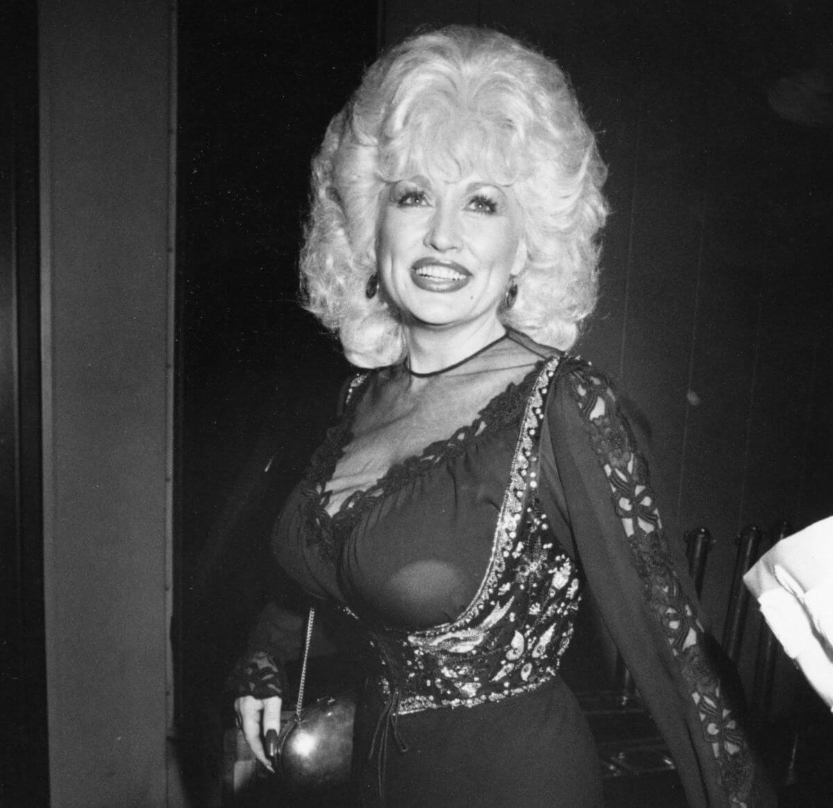 A black and white picture of Dolly Parton wearing a dress with a sheer neckline.