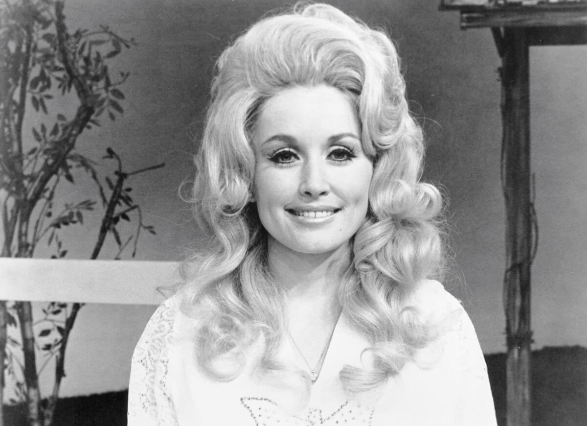 A black and white picture of Dolly Parton sitting in front of a fence.