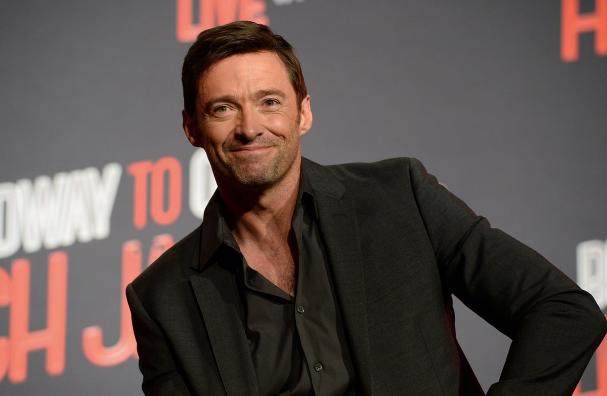 Hugh Jackman with members of the Australian Girls Choir while wearing a black suit.