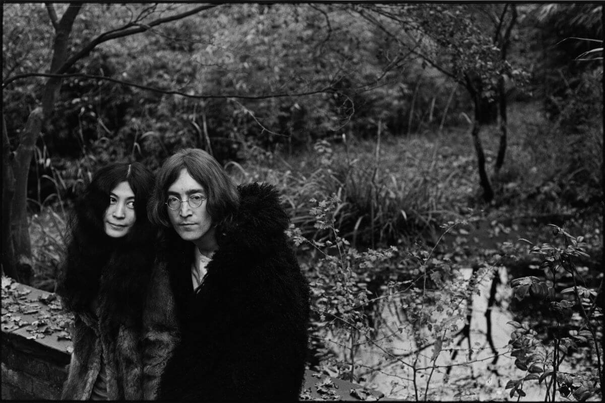 A black and white picture of Yoko Ono and John Lennon standing together on a bridge.