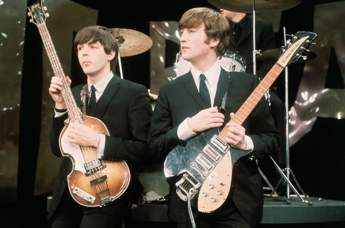 Paul McCartney and John Lennon wear suits and hold guitars.