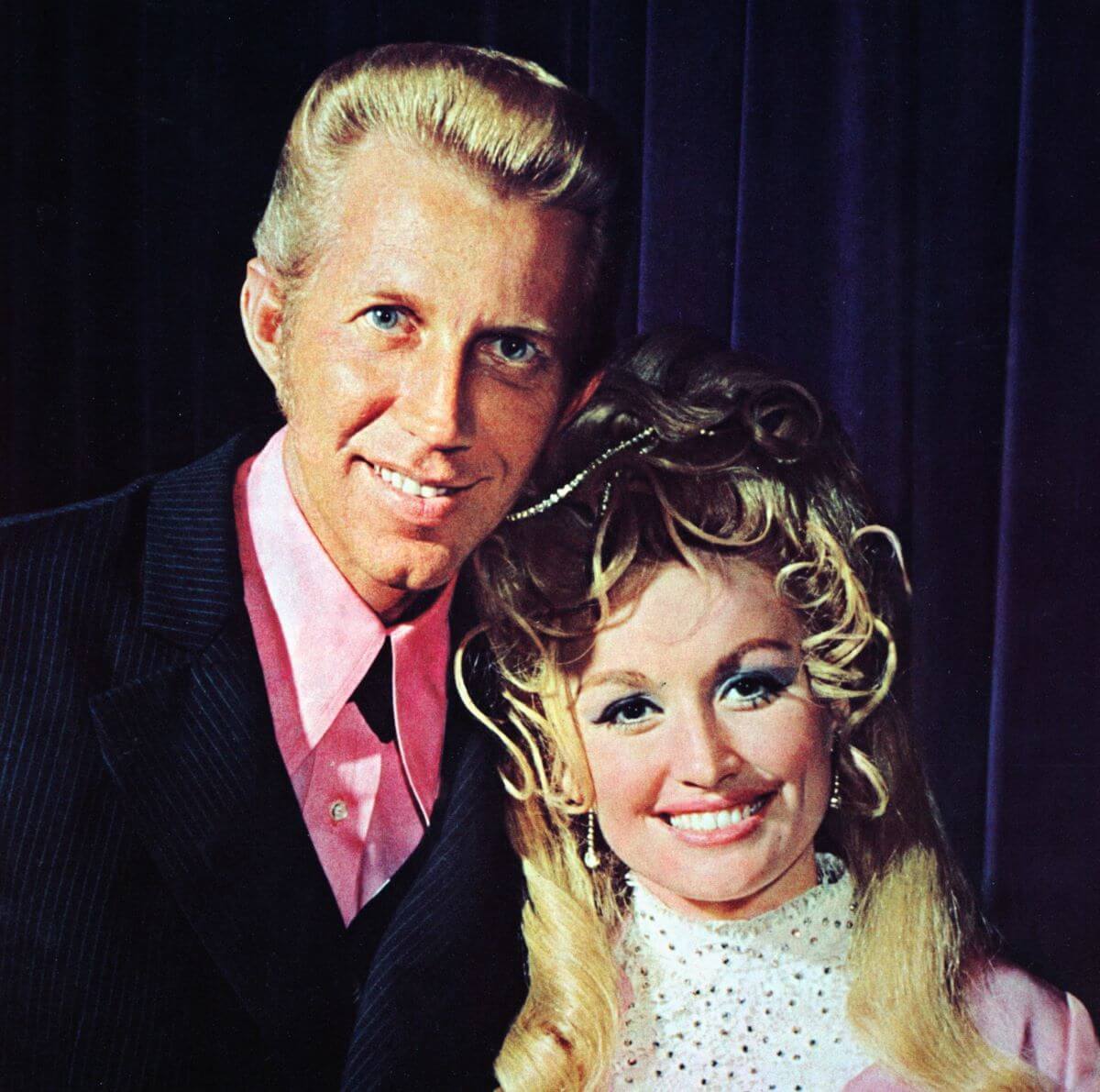 Porter Wagoner and Dolly Parton both wear pink and pose together.