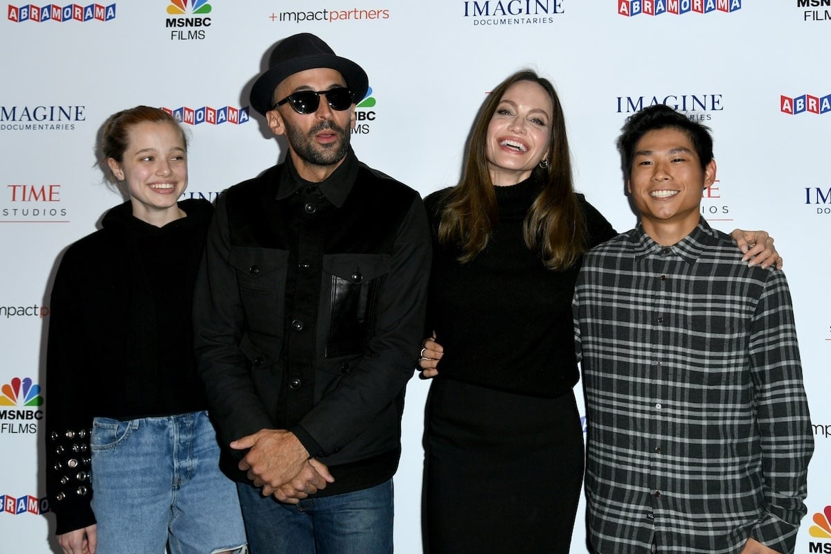Celebrities Shiloh Jolie-Pitt, street artist JR, Angelina Jolie, and Pax Thien Jolie-Pitt stand together on a red carpet
