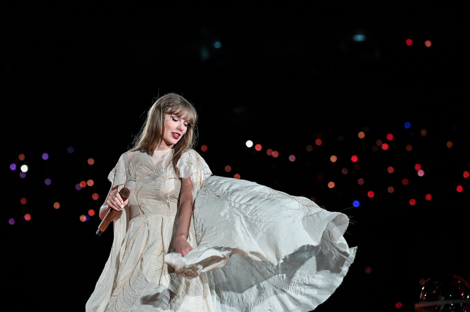 Taylor Swift on stage in Lisbon, Portugal, for 'The Eras Tour' while wearing a flowing white dress and holding a microphone