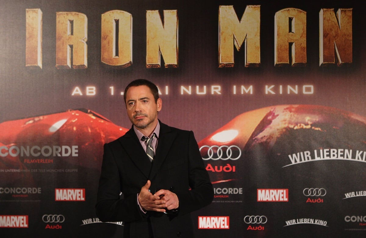 Robert Downey Jr. posing in front of an Iron Man poster while wearing a suit.