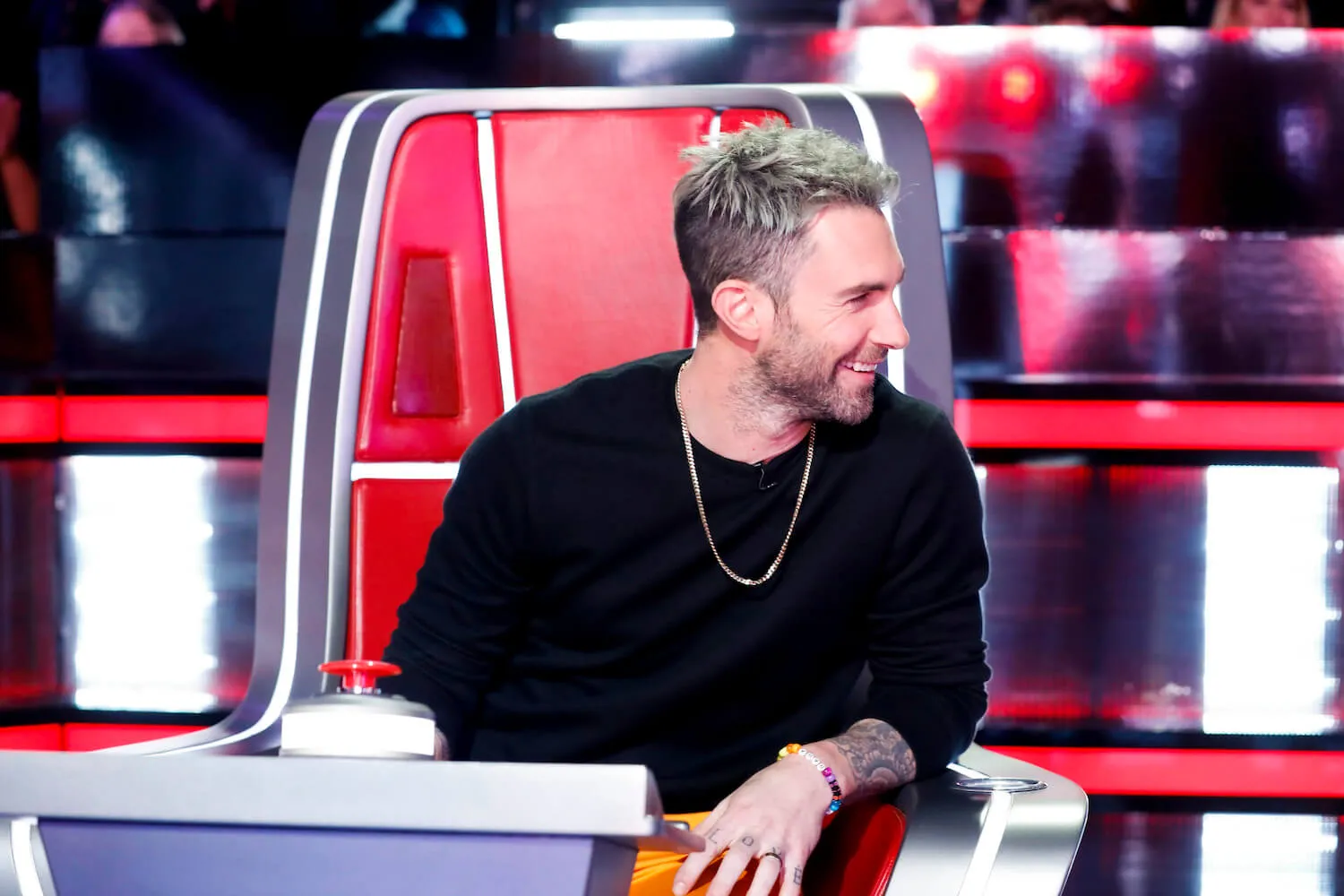 Adam Levine smiling while sitting in a coaching chair on 'The Voice'