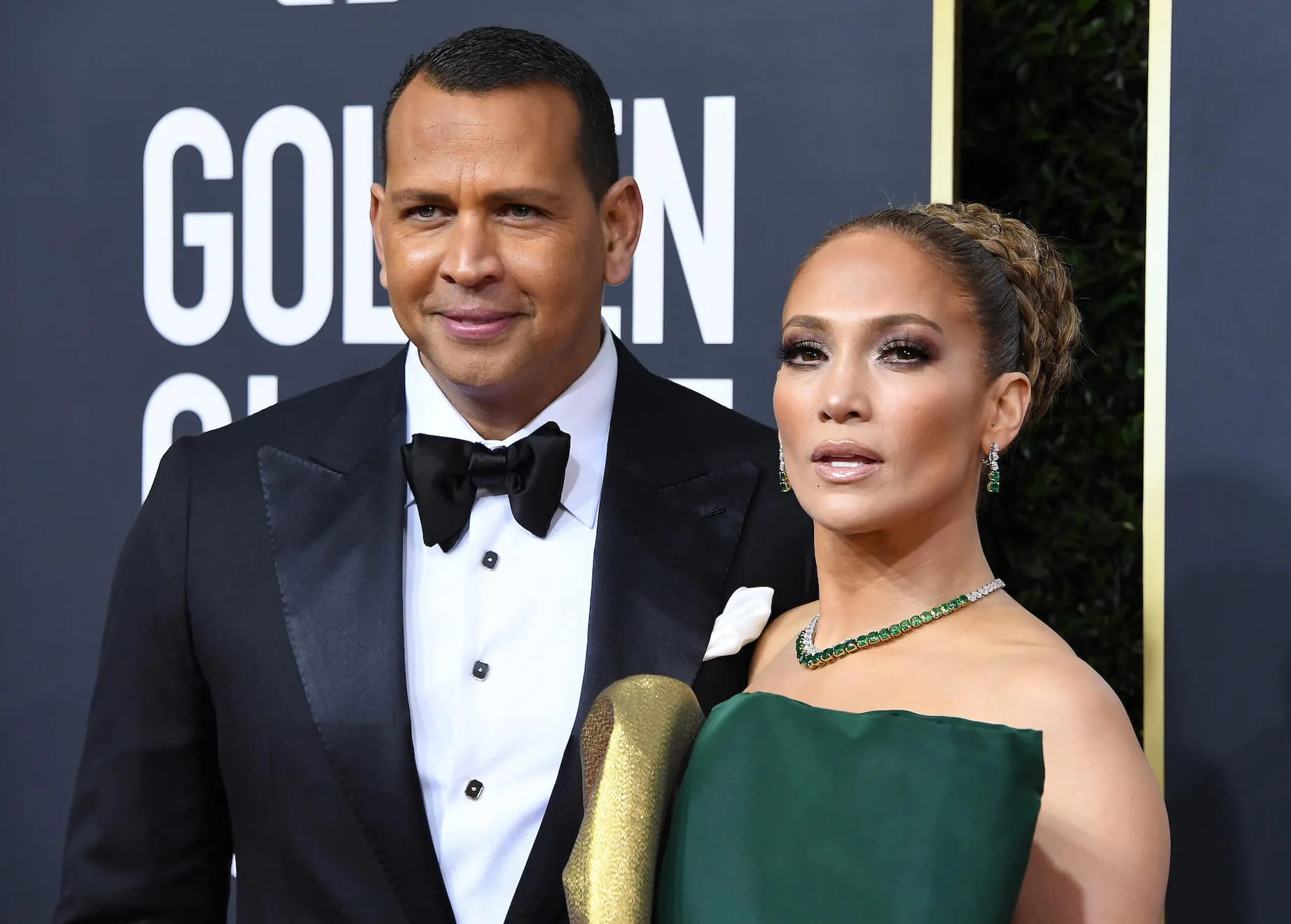 Jennifer Lopez and Alex Rodriguez posing next to each other at the 77th Annual Golden Globe Awards in 2020. Lopez is wearing a green dress and Rodriguez is wearing a tuxedo.