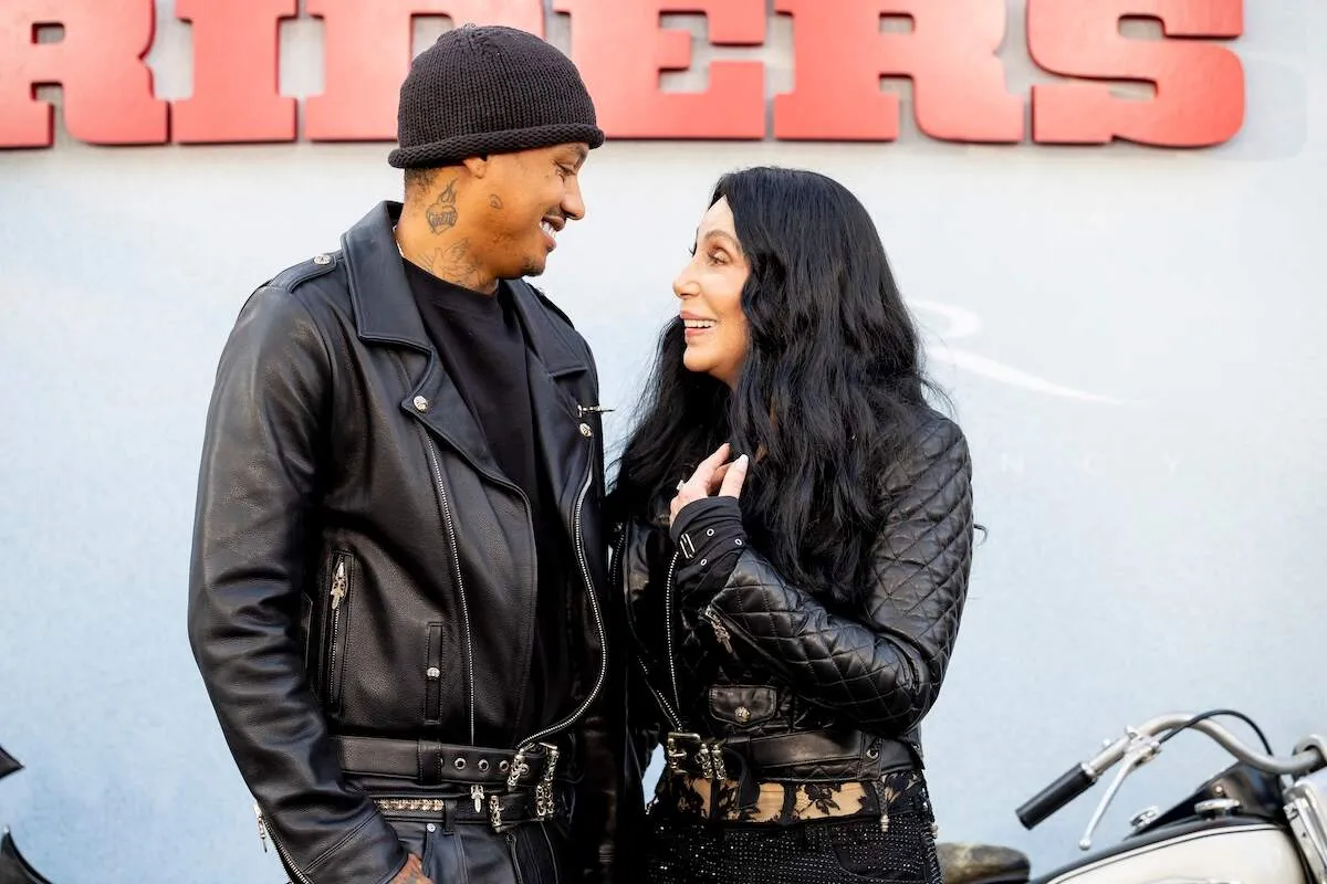 Wearing matching black moto jackets, Alexander Edwards and Cher look at each other on the red carpet