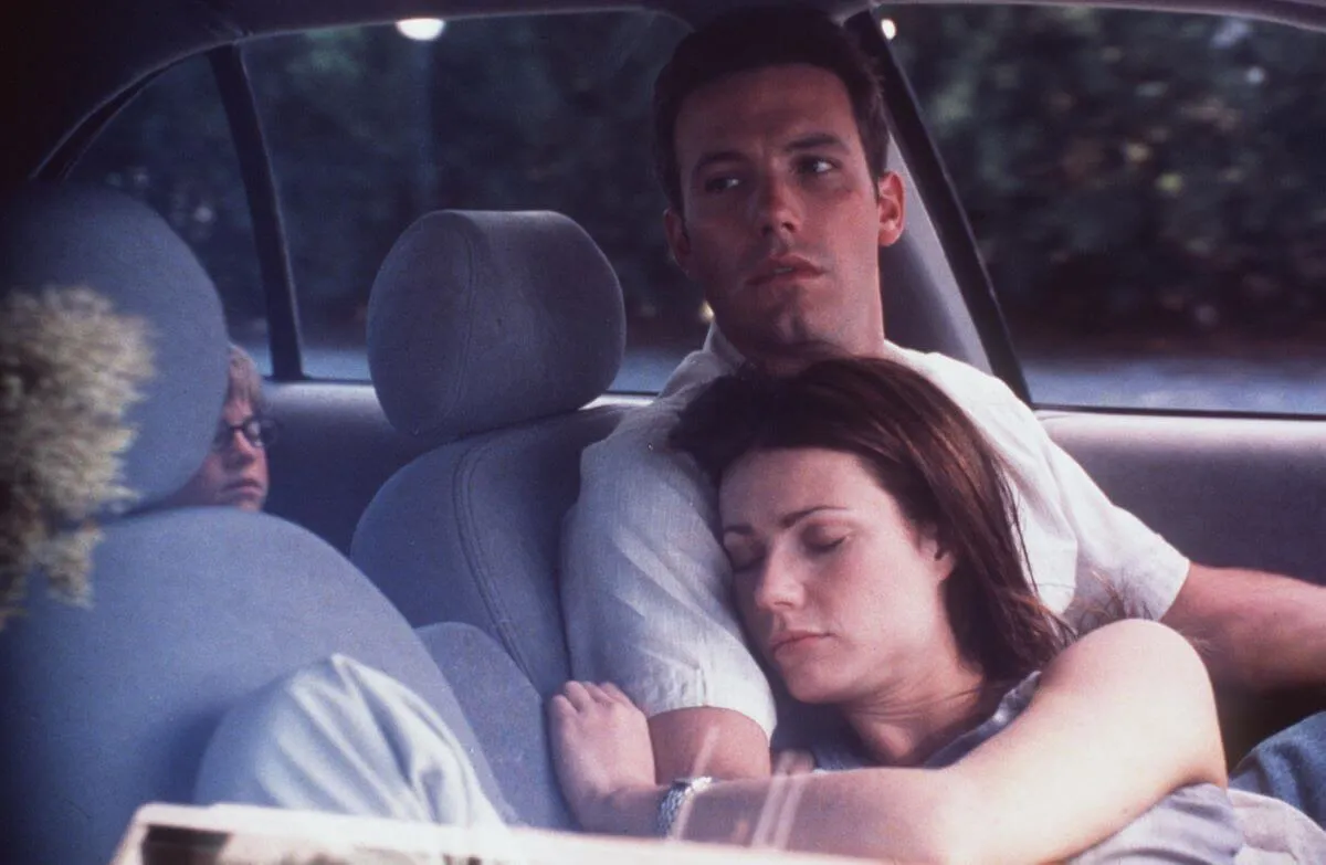 Ben Affleck sits in the drivers seat of a car. Gwyneth Paltrow lays across his chest. A still from the movie 'Bounce.'