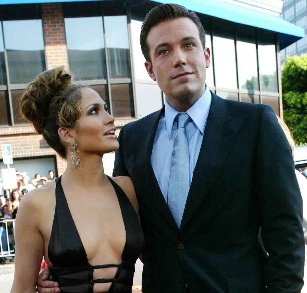 Ben Affleck stands with his arm around Jennifer Lopez. She looks up at him. He wears a suit and she wears a black dress.