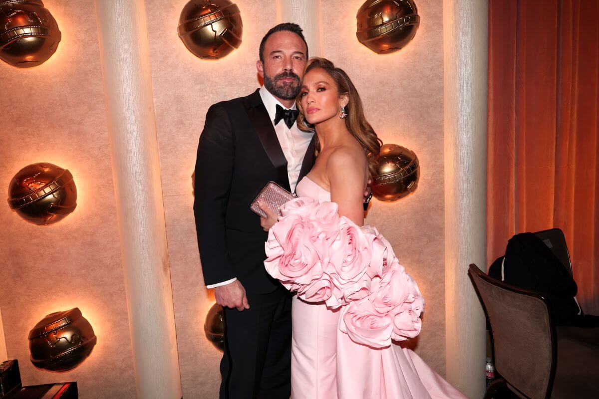 Ben Affleck and Jennifer Lopez pose together on the red carpet. He wears a tuxedo and she wears a pink dress.