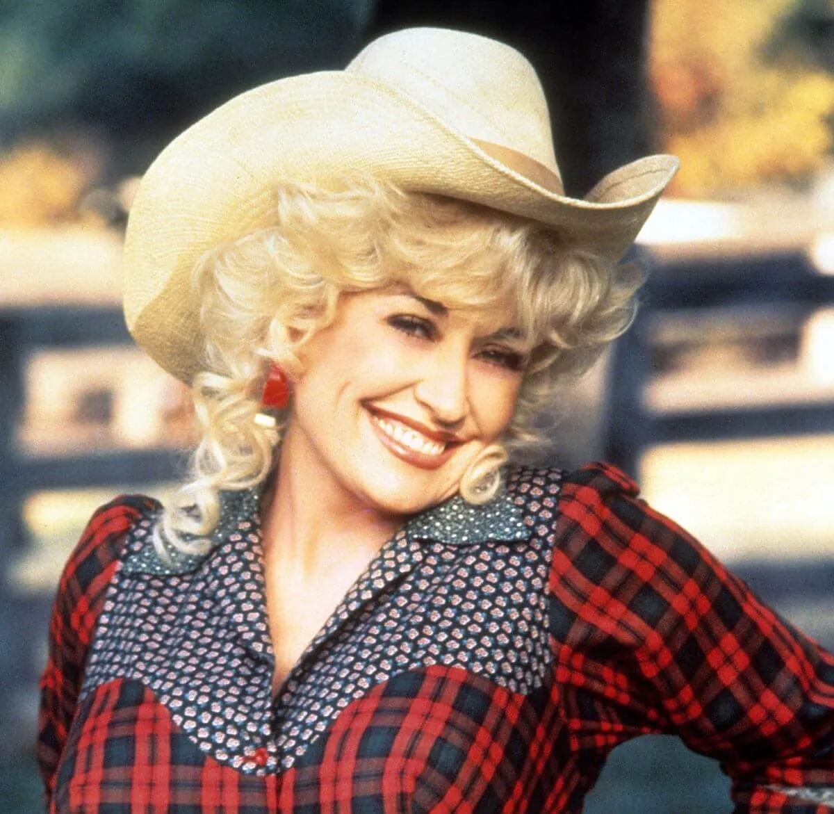 Dolly Parton wears a plaid shirt and a cowboy hat.