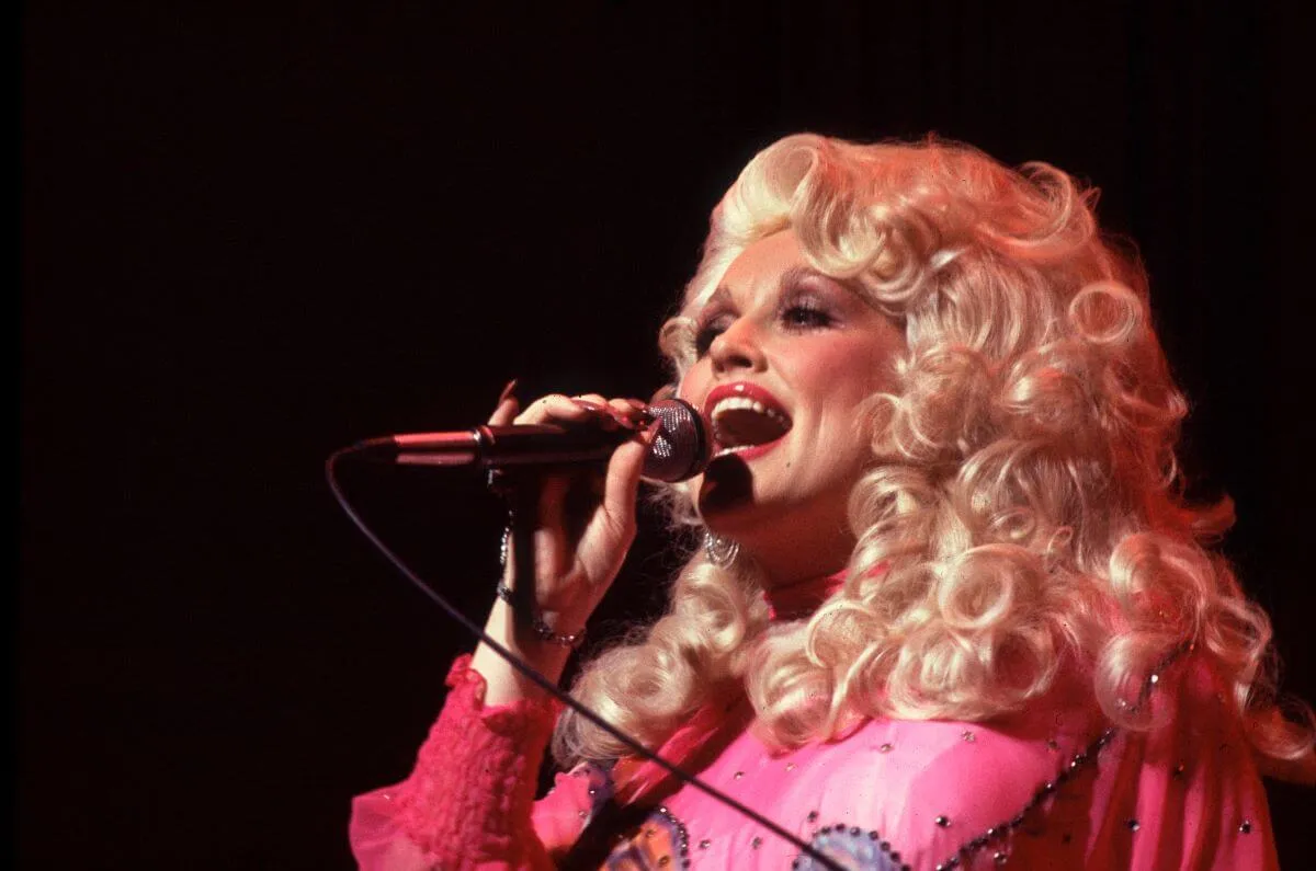 Dolly Parton wears a pink dress and sings into a microphone.