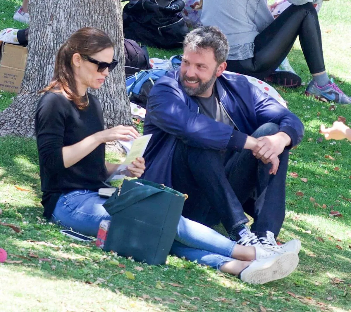 Jennifer Garner and Ben Affleck sit together on the grass under a tree. She wears sunglasses.