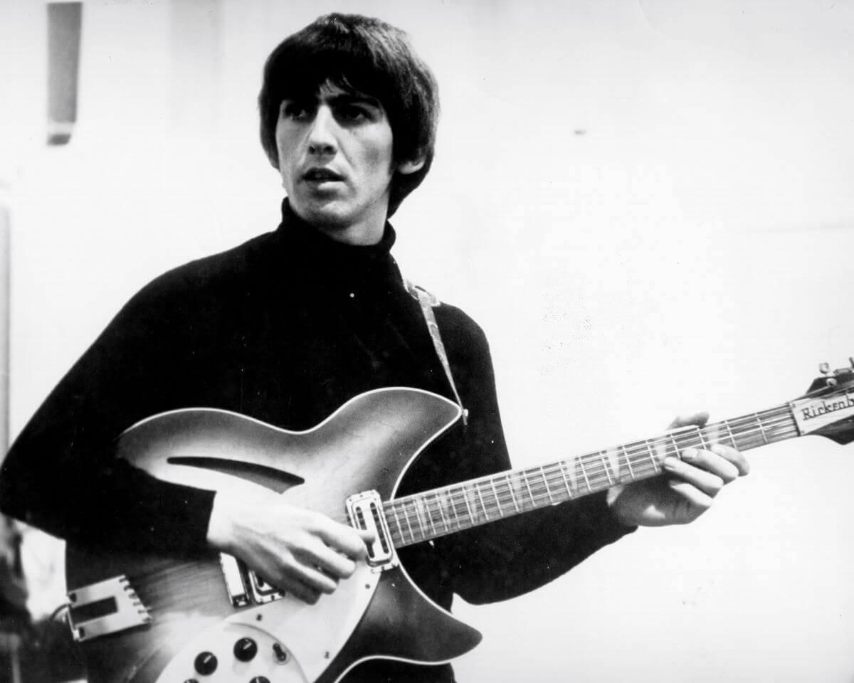 A black and white picture of George Harrison wearing a black turtleneck and playing guitar.