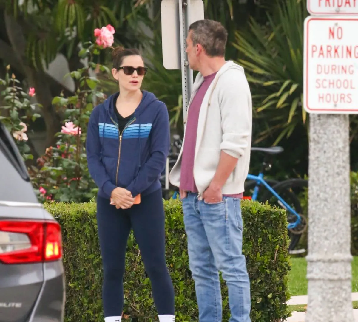 Jennifer Garner and Ben Affleck stand together outside. Jennifer Garner wears a sweatshirt and sunglasses. Ben Affleck wears a sweatshirt and jeans.