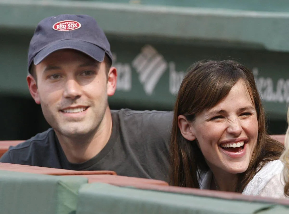 Ben Affleck and Jennifer Garner sit next to each other at a baseball game. He wears a baseball hat.