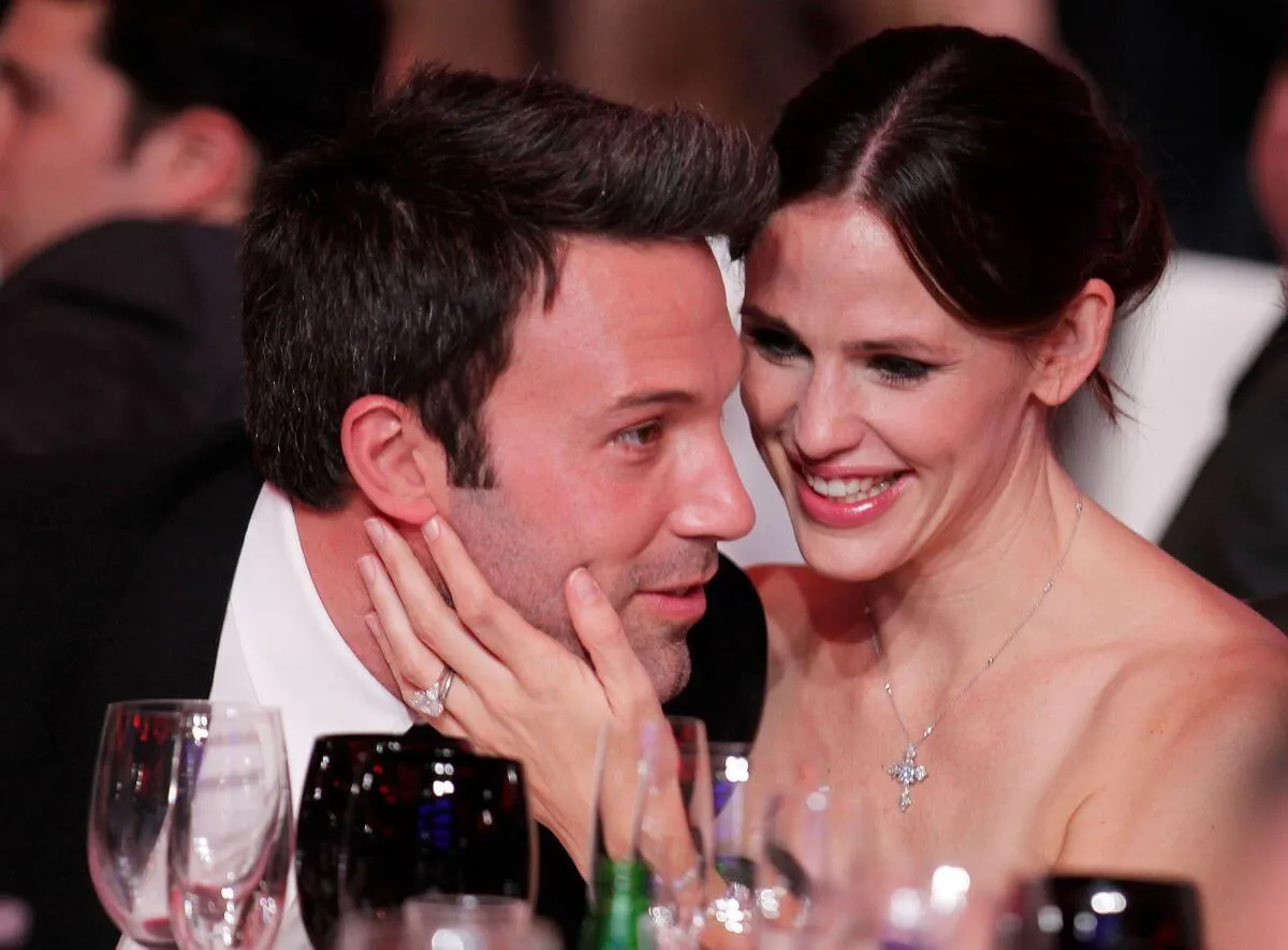 Jennifer Garner and Ben Affleck sit at a dinner table. Affleck leans close to Garner, who touches his face.