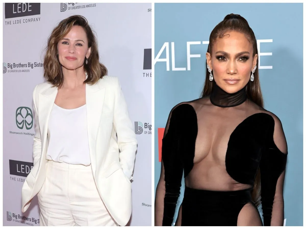 Jennifer Garner wears a white pantsuit and stands with her hands in her pockets. Jennifer Lopez wears a black dress with sheer cutouts.