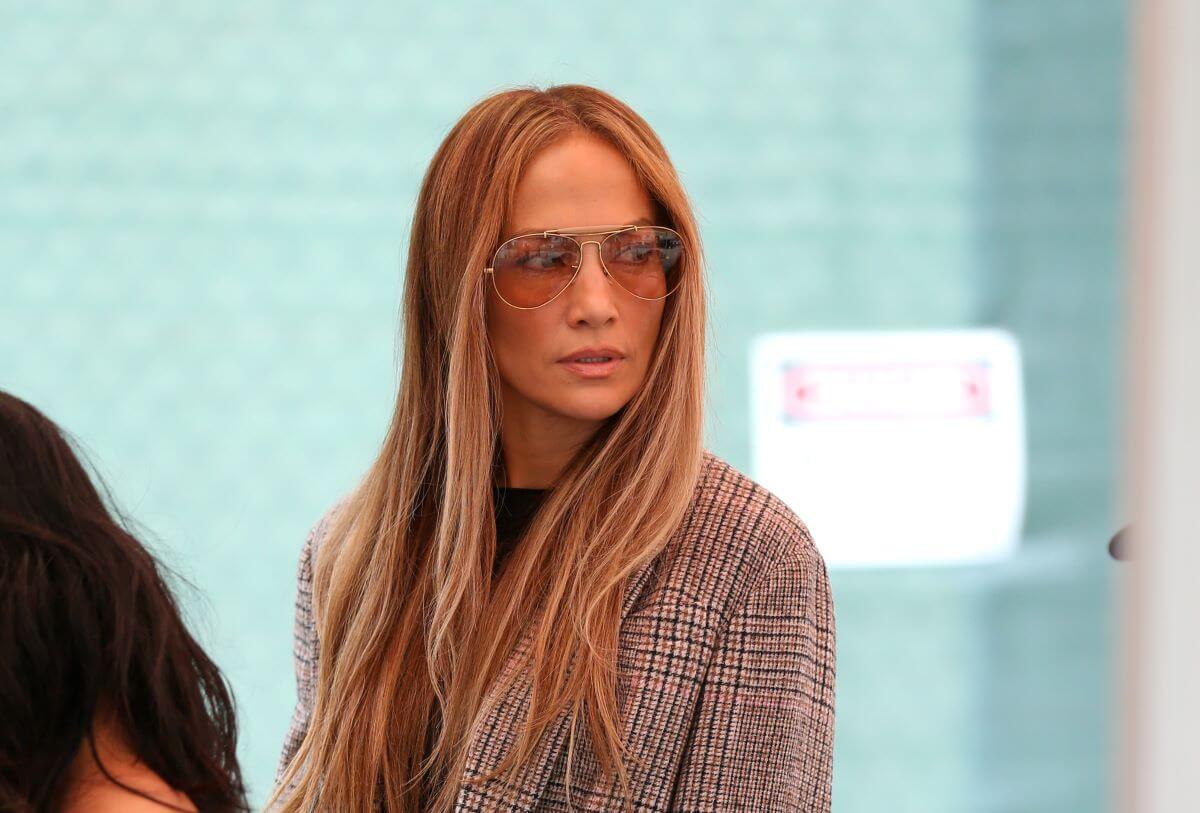 Jennifer Lopez is wearing a plaid blazer and tinted glasses.