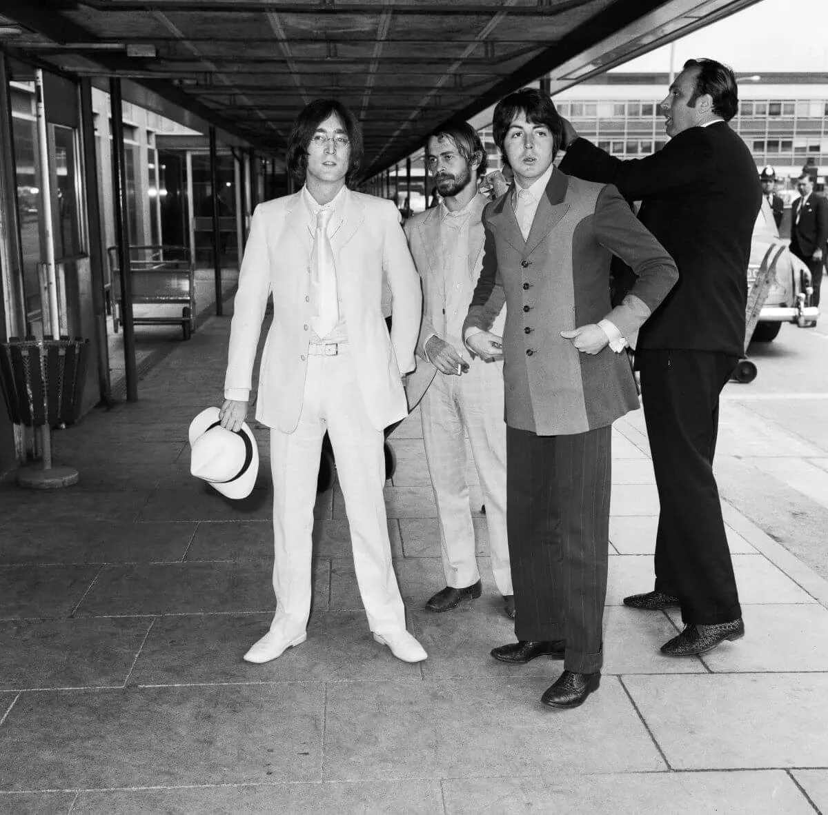 A black and white picture of John Lennon, Alex Mardas, Paul McCartney, and Les Anthony standing outside an airport.