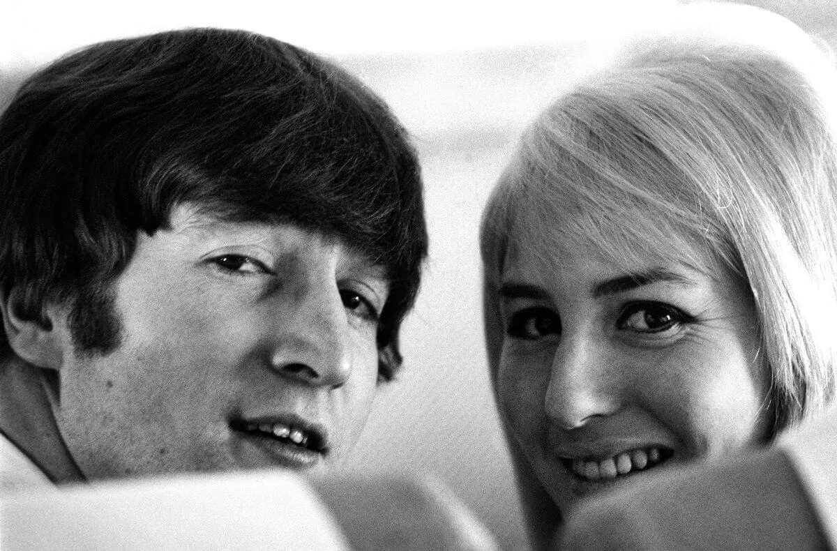 A black and white picture of John and Cynthia looking behind them over chairs.