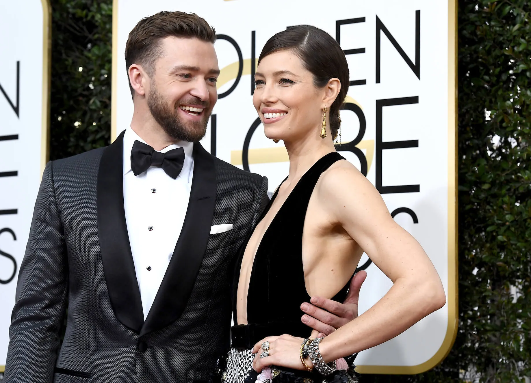 Justin Timberlake and Jessica Biel standing next to each other and smiling at the 74th Annual Golden Globe Awards. Timberlake is wearing a black tuxedo with a bow tie. Biel is wearing a low-cut black dress.