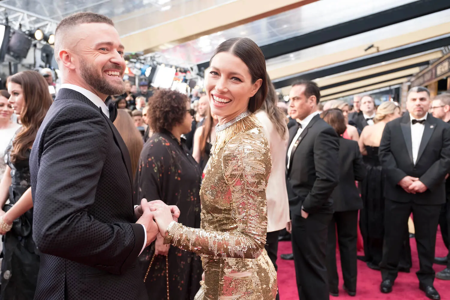 Justin Timberlake holding hands with Jessica Biel while on the red carpet for the 89th Academy Awards. They're both smiling and looking at the camera behind them.
