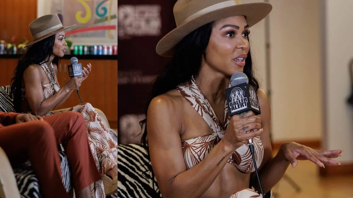 Wearing a tropical bikini-style top and wide leg pants, Meagan Good speaks into a microphone during an interview about Divorce in the Black