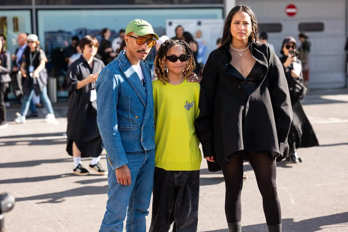 Family members Pharrell Williams, Rocket Williams, and Helen Lasichanh stands outside of a fashion show while wearing edgy outfits